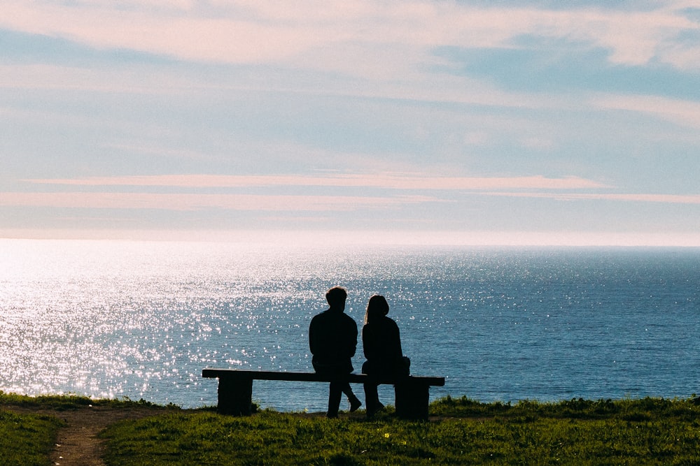 silhouette of man and woman sitting on bench facing sea