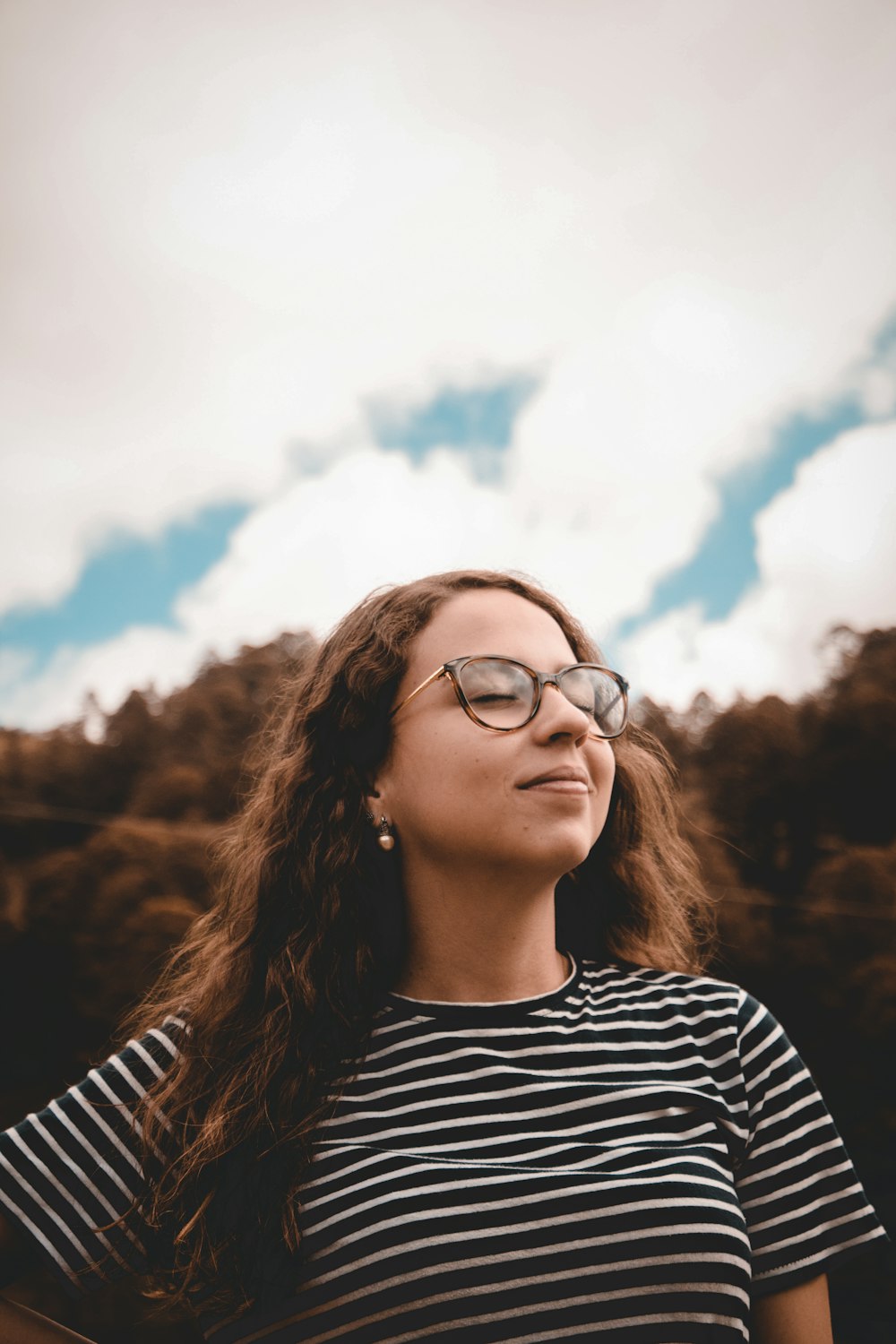 mulher sorridente enquanto fecha os dois olhos usando óculos sob nuvens brancas