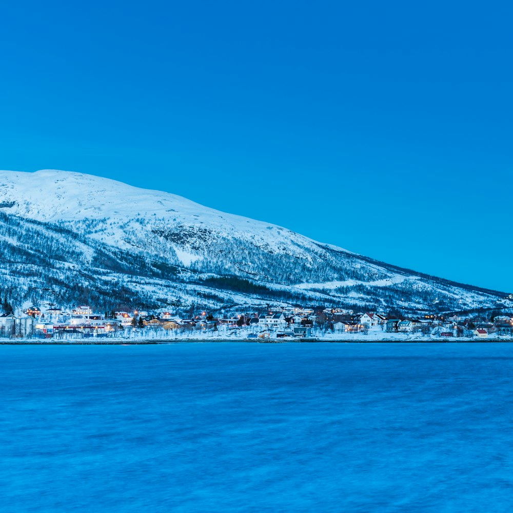 snow covered mountain near calm body of water