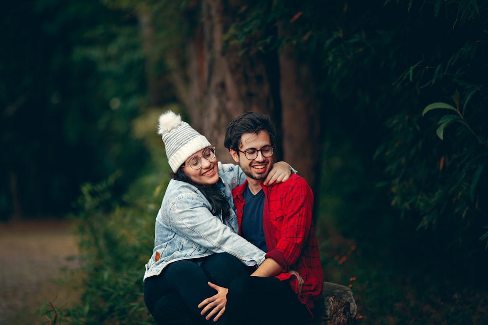 woman wearing bobble hat sitting on man's lap near tree