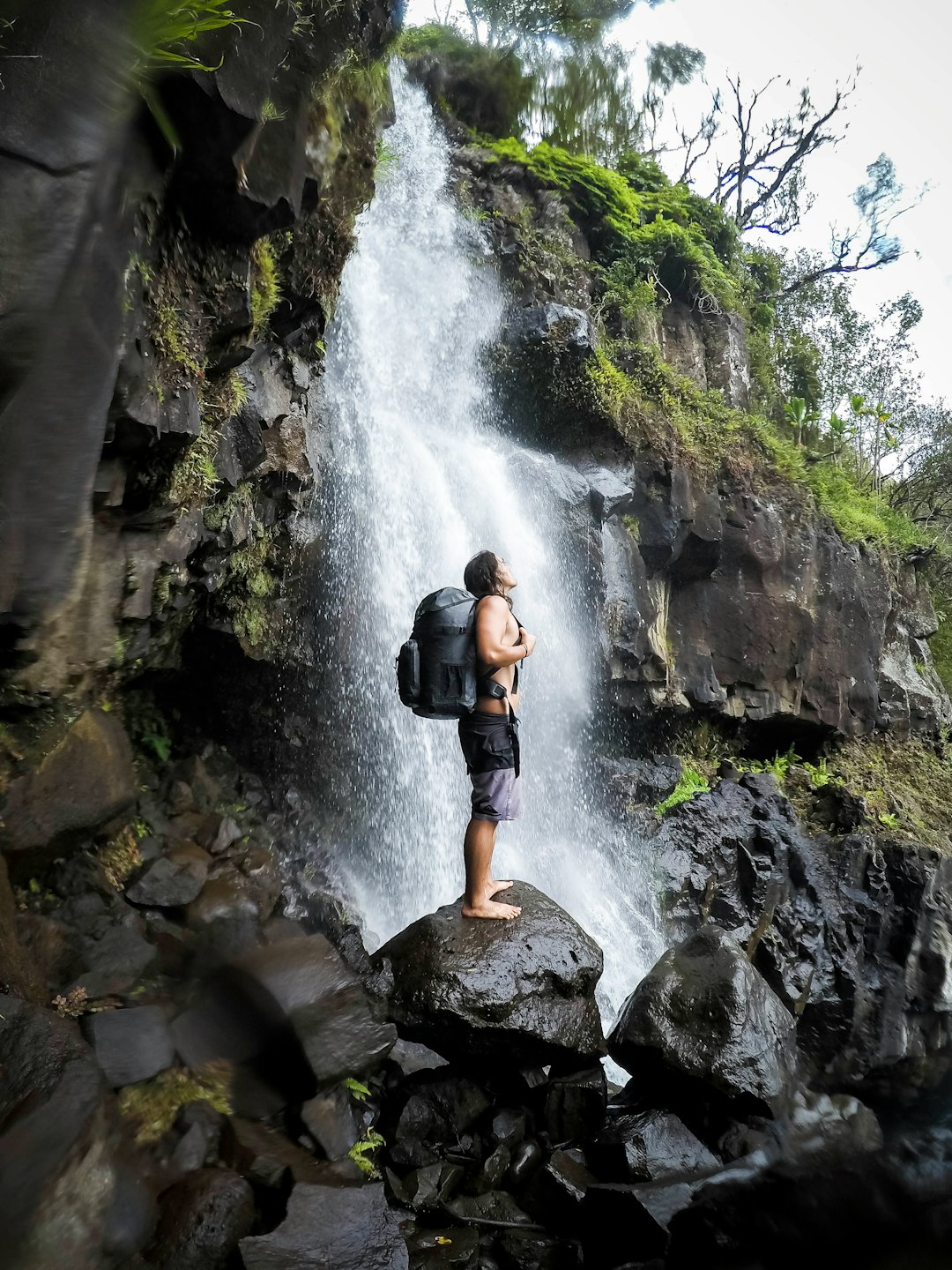 man carrying rucksack backpack standing on stone on front of waterfalls