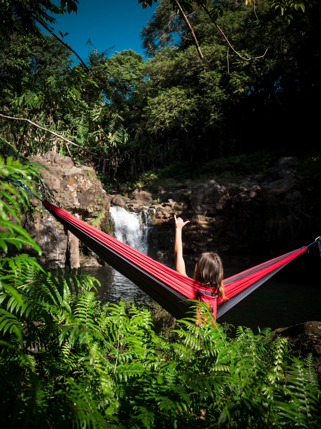 woman sitting on red and black hammock near waterfalls during daytime
