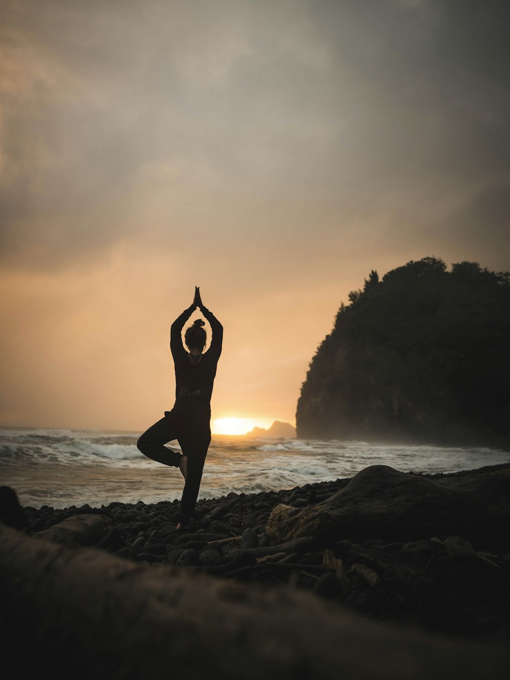 woman doing one-foot yoga stance at the beach under grey sky