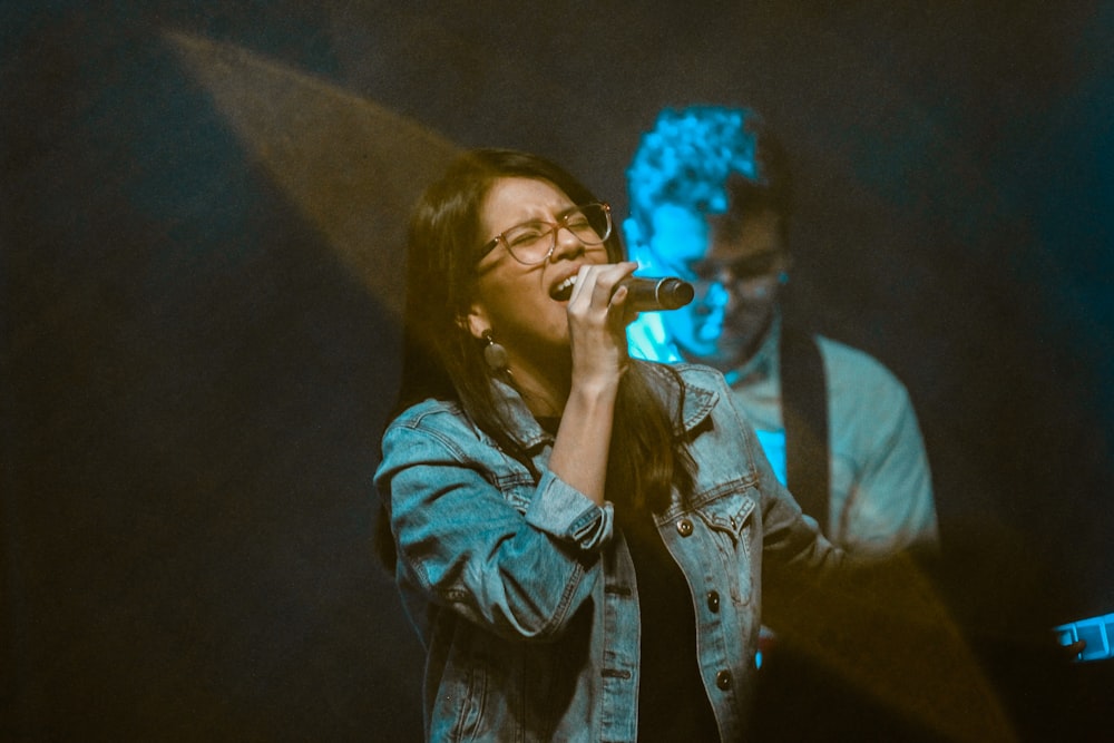 woman wearing blue denim jacket singing near man playing guitar