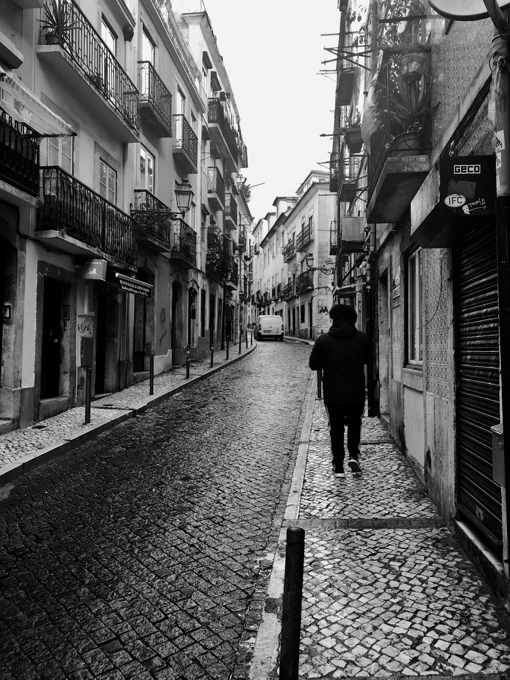 grayscale photo of man on sidewalk between buildings