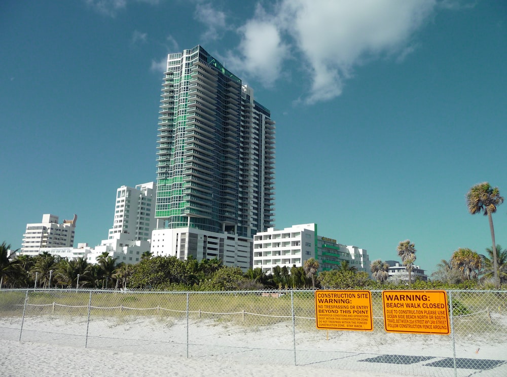 two yellow warning signs on fence near curtain-wall high-rise building