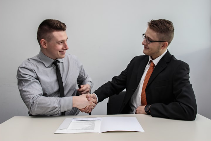 two agents handshaking over a referral agreement at a table dressed in business casual 