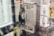 A vintage public payphone with a corded handset is mounted on a wall inside a phone booth. The metallic casing of the phone is slightly worn and aged. Several colorful advertisements with images are posted around the phone, promoting various services.