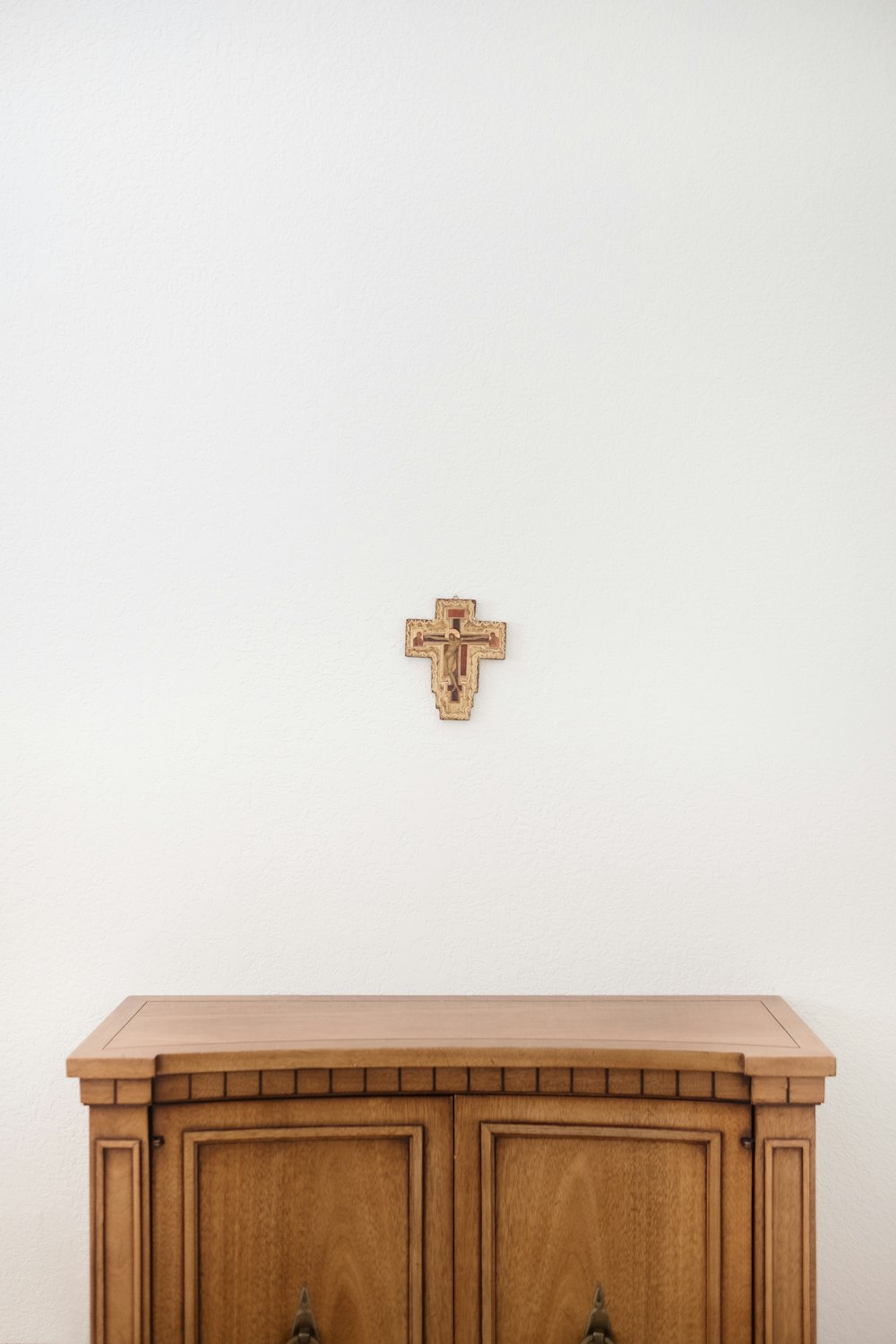 brown cross on wall above brown wooden sideboard