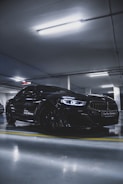 A sleek black sports car parked under moody dark blue lighting in a modern garage.