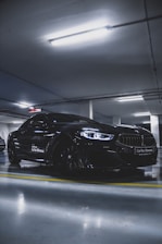 A sleek black sports car parked under moody dark blue lighting, reflecting the modern and premium vibe of Car Guys.