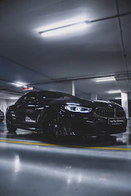 A sleek black sports car parked in a futuristic industrial garage with moody lighting.