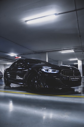 A sleek black sports car parked under moody dark blue lighting, reflecting the modern and premium vibe of Car Guys.