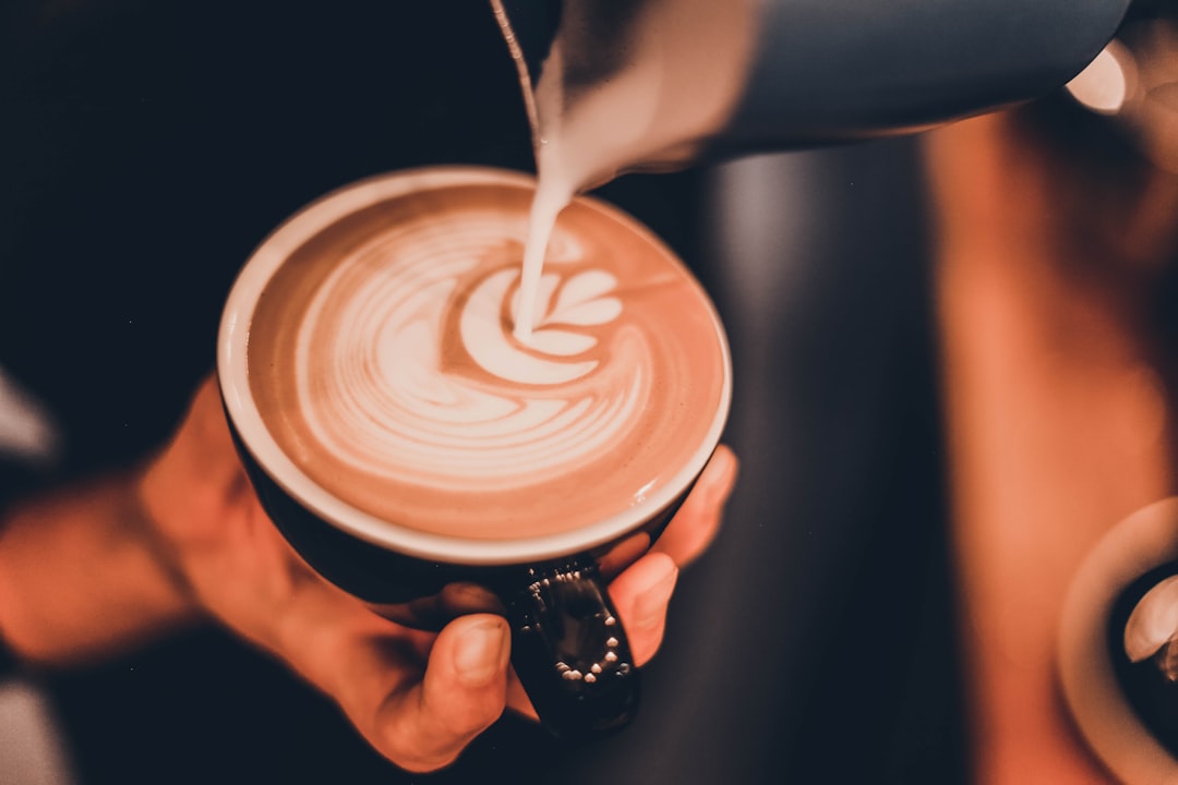 person pouring milk on coffee cup