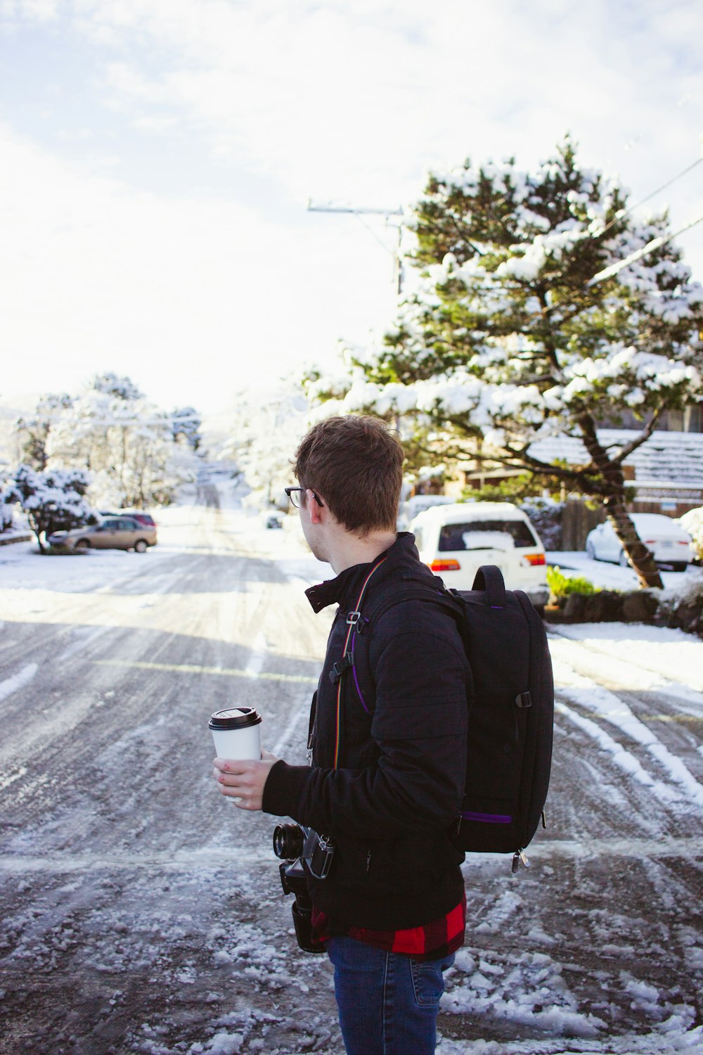 man holding cup of coffee wearing backpack leaning on vehicle during daytime