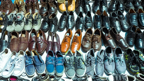 A diverse collection of shoes arranged neatly in rows, showcasing various styles and colors such as sneakers, leather shoes, and sandals. The shoes vary in shades from browns and blacks to blues and whites.