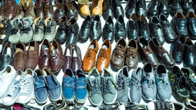 A diverse collection of shoes arranged neatly in rows, showcasing various styles and colors such as sneakers, leather shoes, and sandals. The shoes vary in shades from browns and blacks to blues and whites.