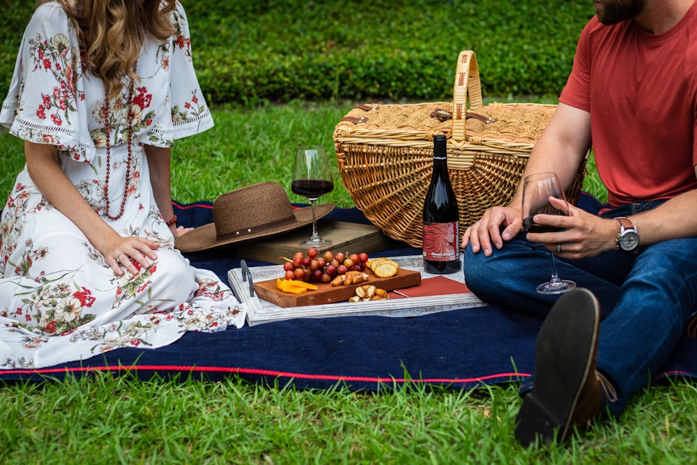 man and woman sitting on blue textile beside brown wicker picnic basket