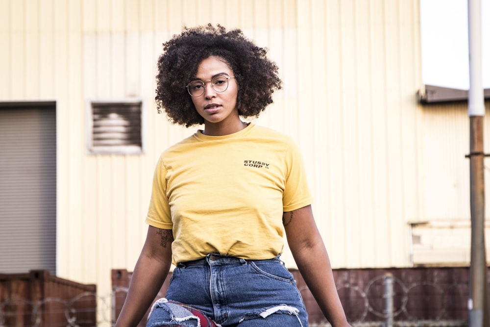 woman wearing yellow crew-neck shirt sitting near white concrete building during daytime