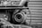 A close-up view of an industrial machine component, possibly a turbocharger or similar machinery part. The metal surfaces appear weathered, with visible wear, rust, and texture. The background consists of horizontal, corrugated metal resembling a garage door or industrial wall.
