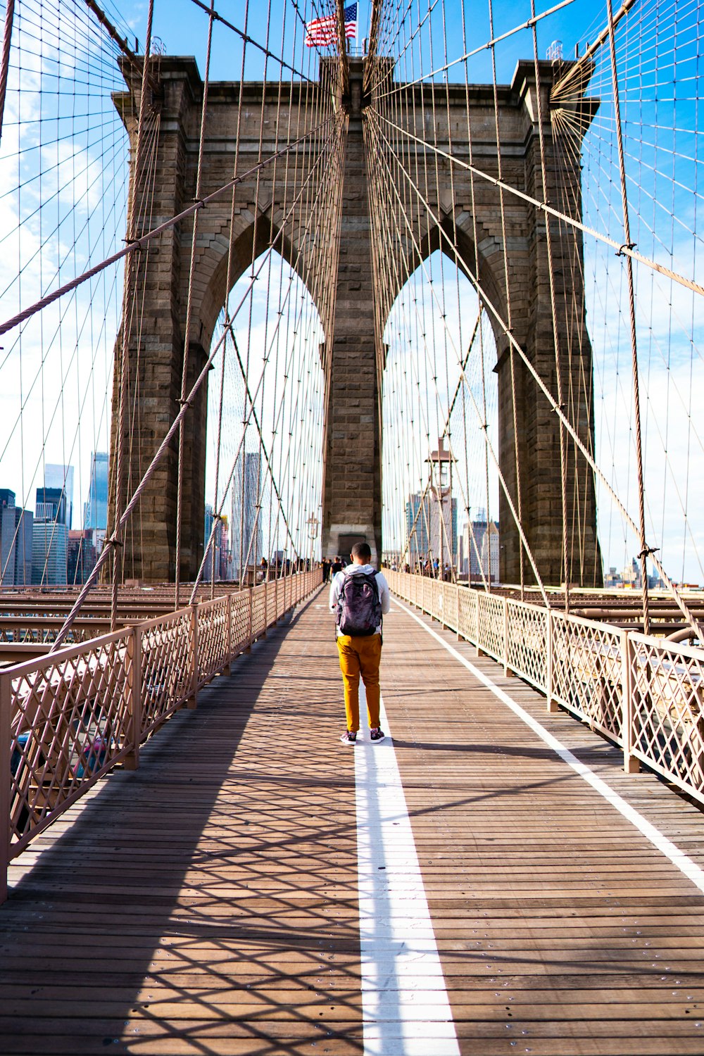 Un hombre con camisa blanca y pantalones amarillos caminando por el puente durante el día.