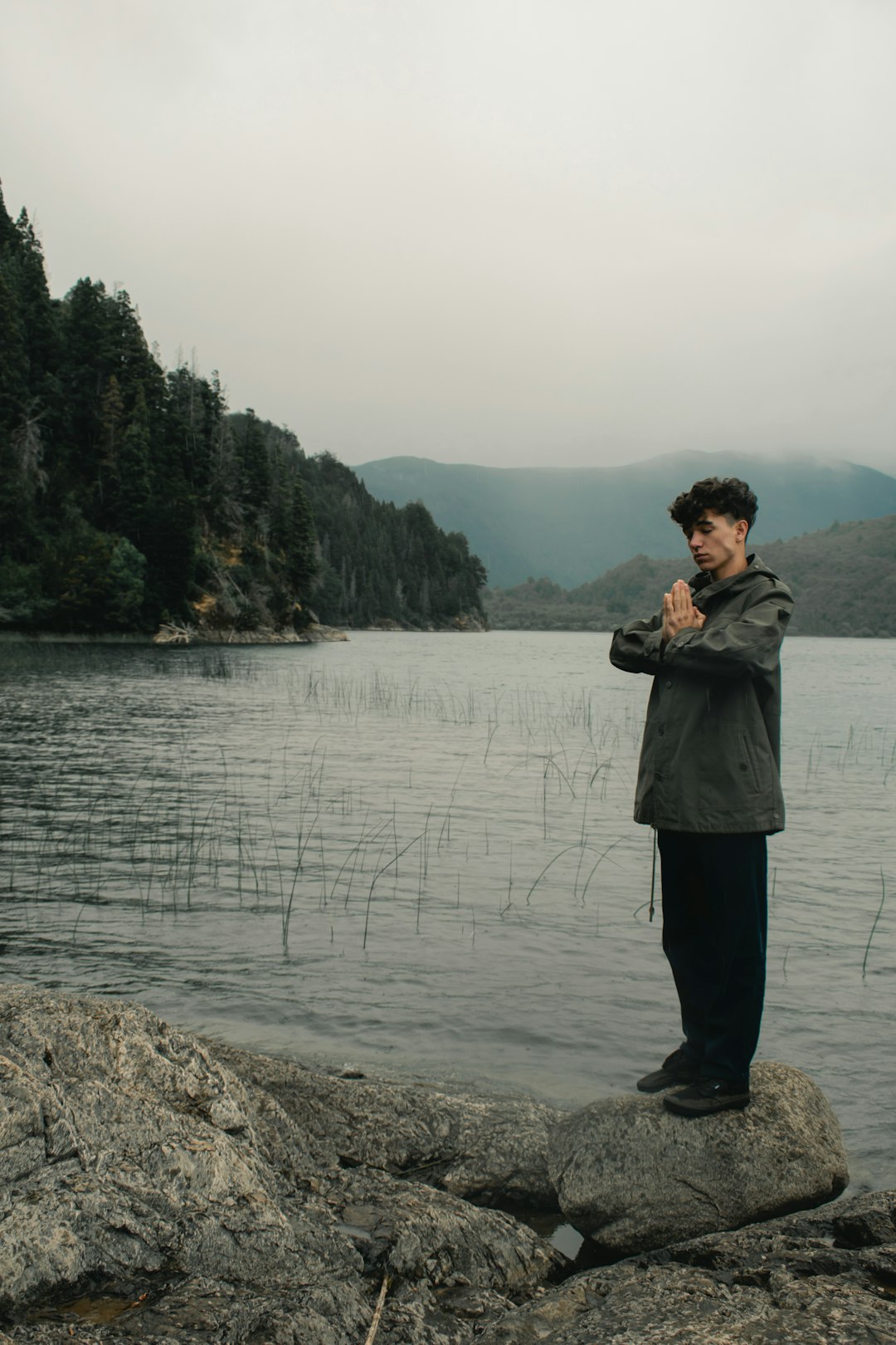 man standing and meditating on rock beside body of water during daytime