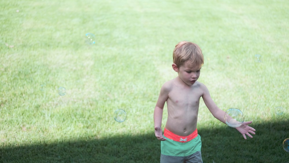 topless boy standing on green grass