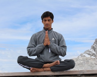 man meditating on brown wooden platform during daytime