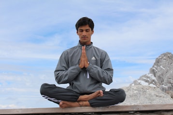 man meditating on brown wooden platform during daytime