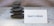 A small stack of smooth, dark stones is arranged neatly on a textured surface. Next to the stones is a white card displaying the text 'Expect A Miracle' in blue letters. The background has a subtle wavy pattern, adding to the calm and serene atmosphere of the scene.