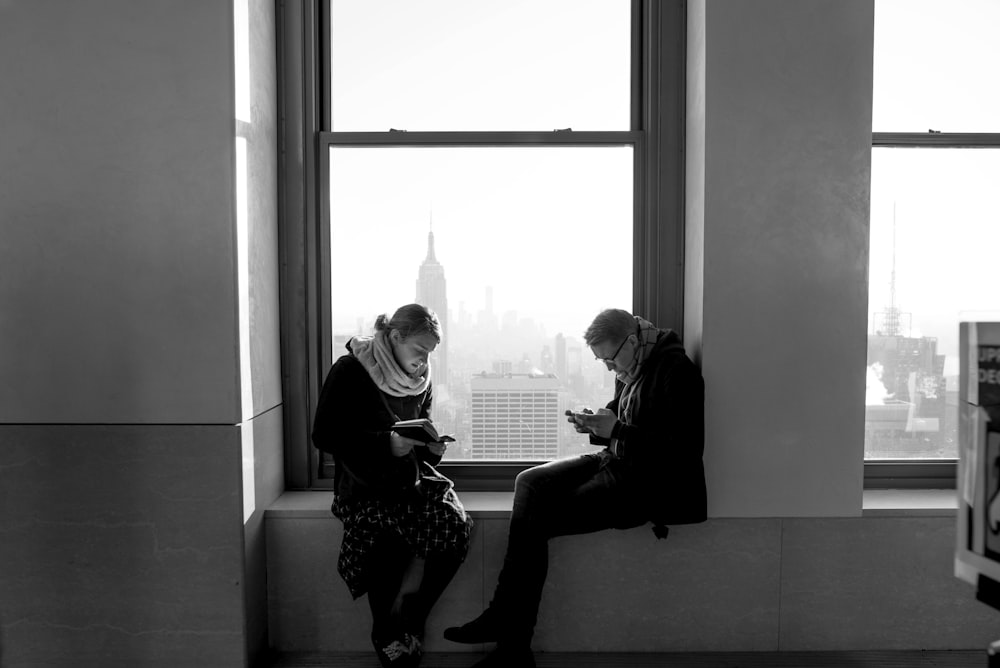 man and woman sitting near window inside building