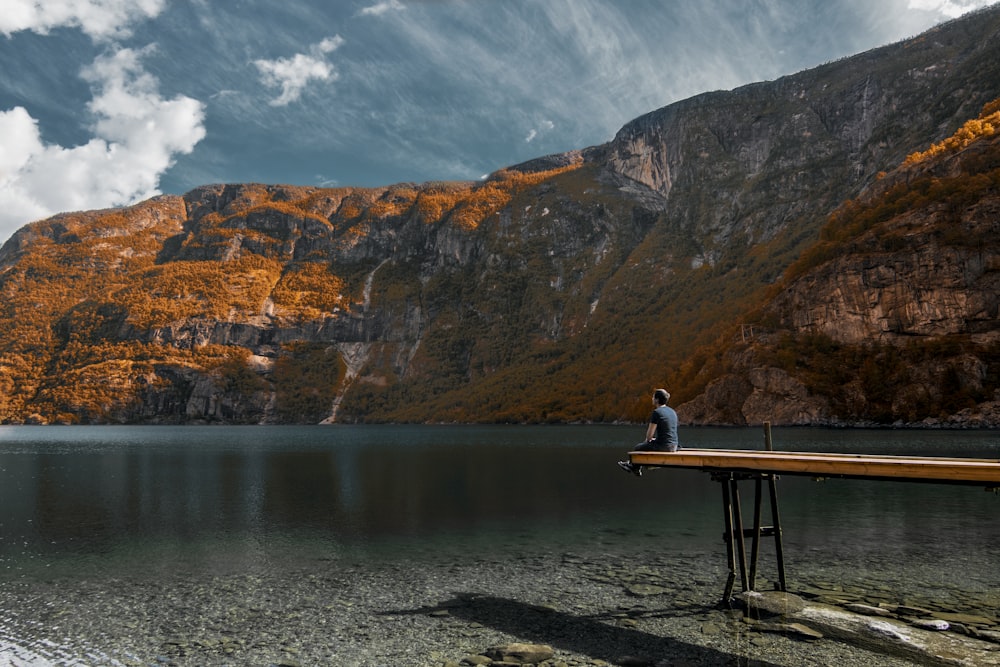 man in black top sitting on wooden dock