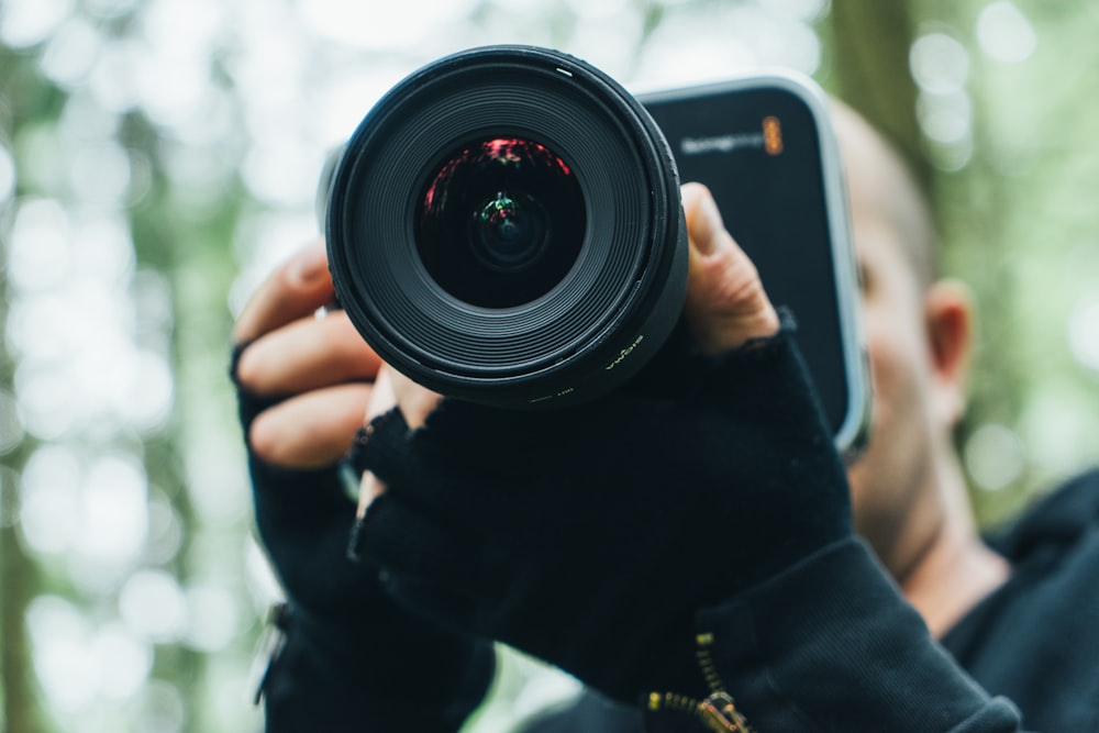 person holding camera while standing near forest trees