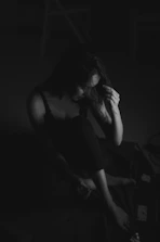 Softly lit image of a woman sitting alone, lost in thought, surrounded by shadows.