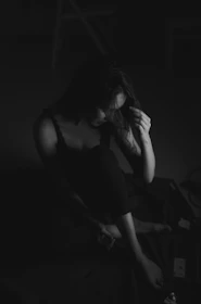 Softly lit image of a woman sitting alone, lost in thought, surrounded by shadows.