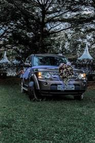 A festive car decorated with elegant flowers parked outside a wedding venue at sunset.