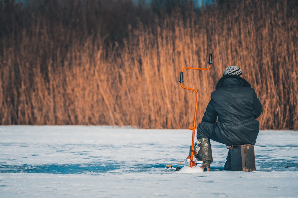 person sitting near auger drill in field covered with snow