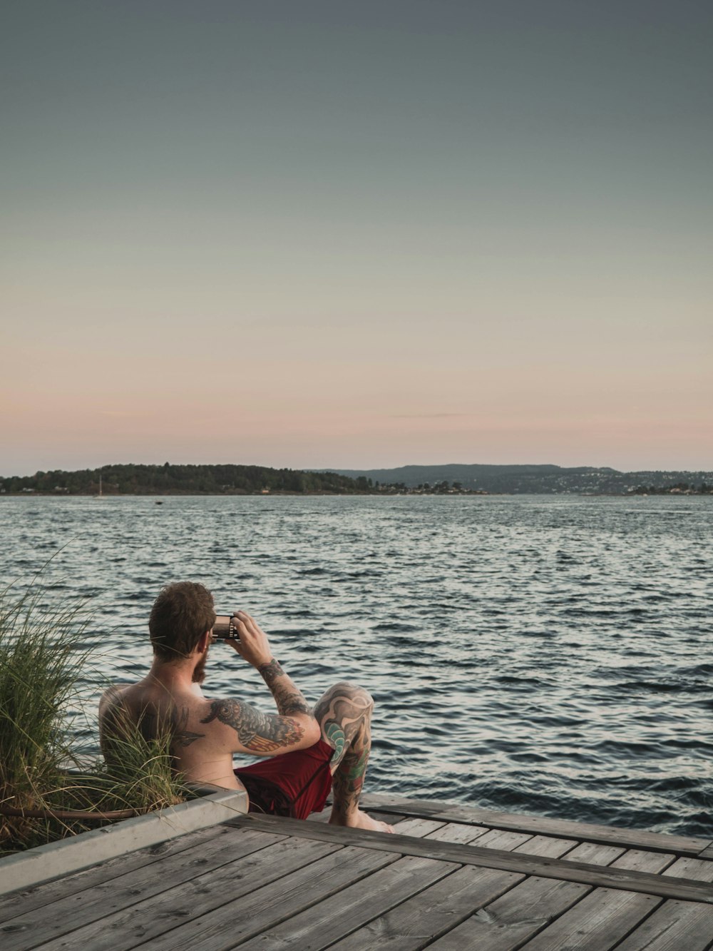 man in red shorts sitting in front of body of water