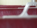 A close-up image of the textured surface of a red leather material with visible wear and tear, focused between smooth, white plastic armrest structures.
