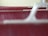 A close-up image of the textured surface of a red leather material with visible wear and tear, focused between smooth, white plastic armrest structures.