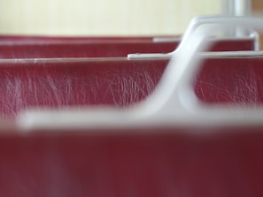 A close-up image of the textured surface of a red leather material with visible wear and tear, focused between smooth, white plastic armrest structures.
