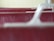 A close-up image of the textured surface of a red leather material with visible wear and tear, focused between smooth, white plastic armrest structures.