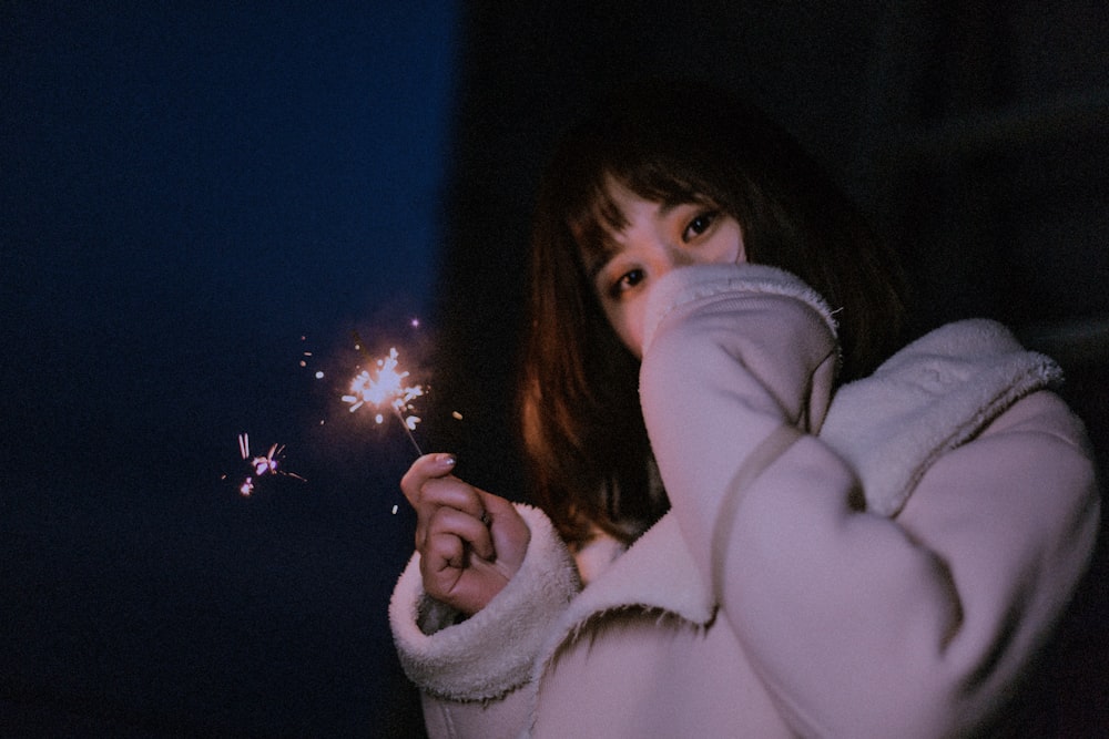 woman holding sparkler light in dark surface