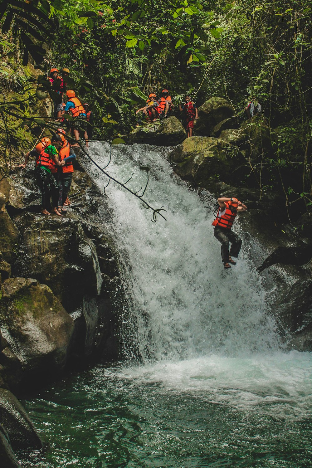 person wearing personal floating devices jumps beside waterfalls