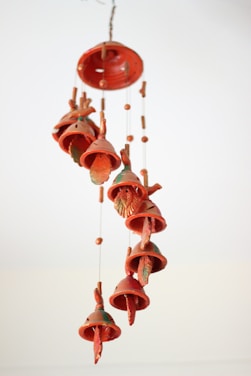 A collection of terracotta wind chimes hangs from strings, each shaped like a bell with leaf designs and small beads interspersed among them. The chimes have a warm, earthy orange hue with green accents.