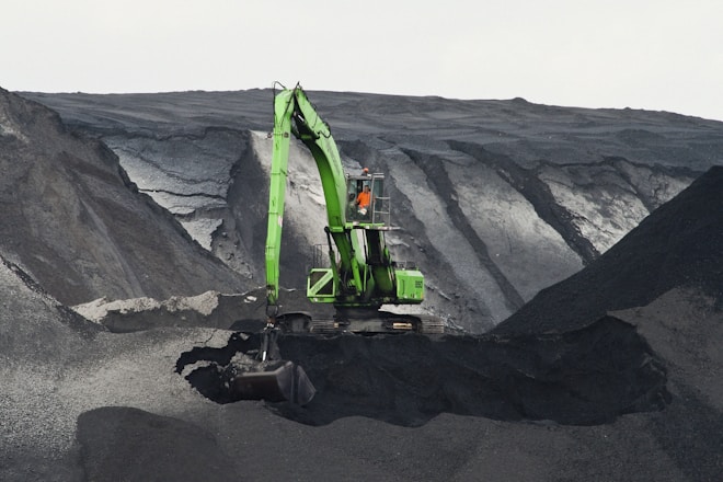 green backhoe digging hole in the middle of mountain