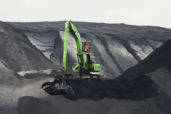 green backhoe digging hole in the middle of mountain
