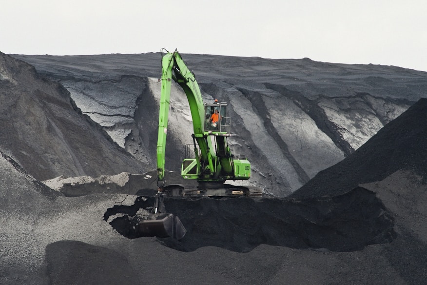 green backhoe digging hole in the middle of mountain