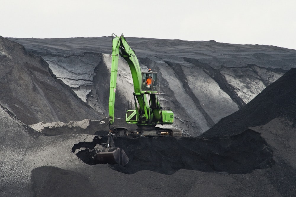 Grüner Bagger gräbt Loch in der Mitte des Berges