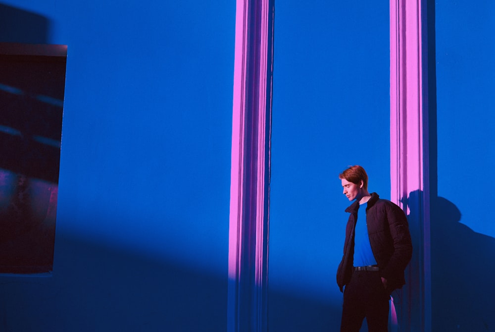 man in black full-zip jacket standing near blue wall